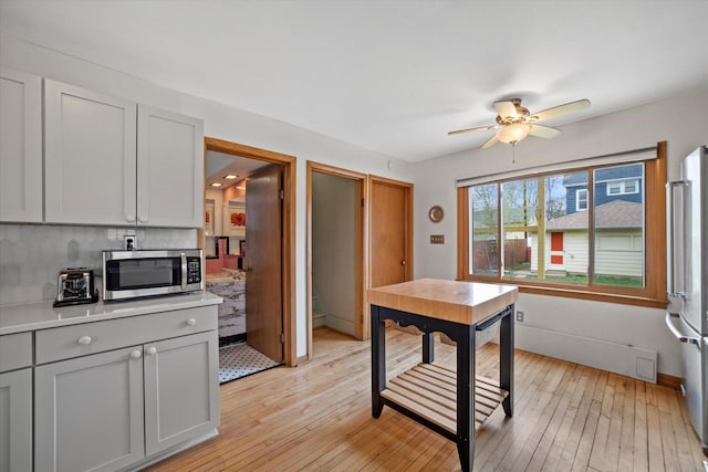kitchen with ceiling fan, light countertops, light wood-style flooring, stainless steel appliances, and decorative backsplash