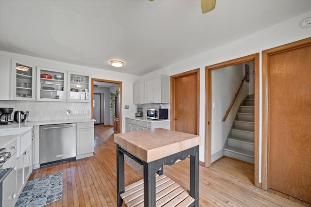 kitchen featuring stainless steel appliances, decorative backsplash, glass insert cabinets, and light wood-type flooring