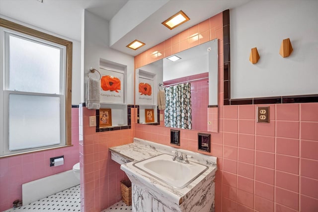 bathroom featuring vanity, toilet, a shower with shower curtain, a wainscoted wall, and tile walls