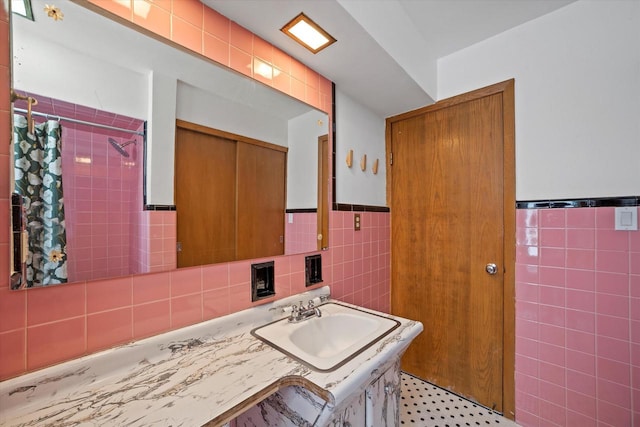 full bathroom featuring a sink, tile walls, wainscoting, and tiled shower