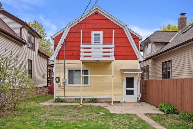 view of front facade featuring a gambrel roof, a front lawn, fence, and a balcony