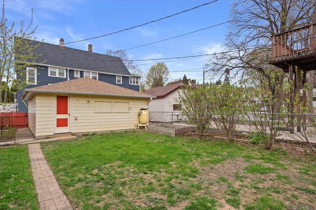 back of house with a lawn, a garden, fence, and roof with shingles