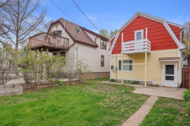back of house with fence, a gambrel roof, a balcony, a lawn, and a patio