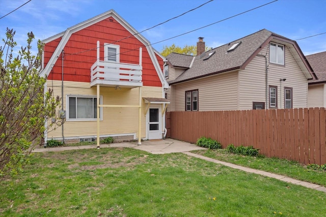 back of property featuring fence, roof with shingles, a gambrel roof, a balcony, and a yard