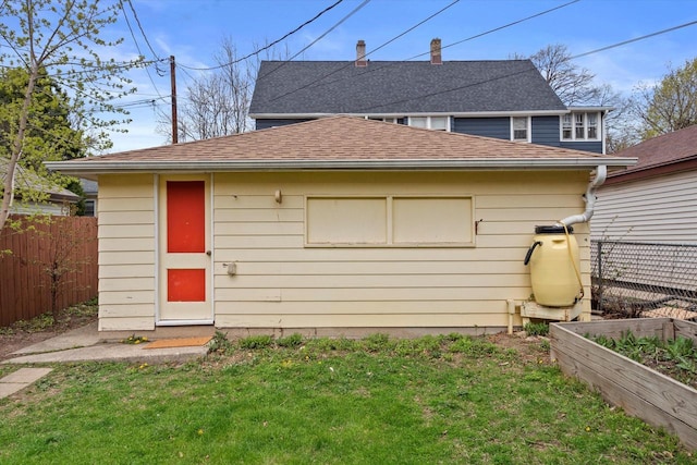 rear view of house featuring a shingled roof, fence, a yard, and a vegetable garden