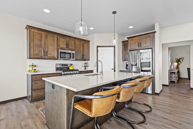 kitchen with baseboards, light countertops, a sink, light wood-style flooring, and stainless steel appliances