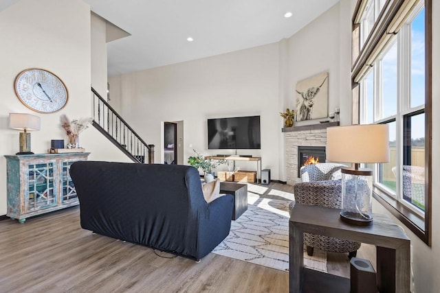 living room featuring a fireplace, stairs, recessed lighting, wood finished floors, and a towering ceiling