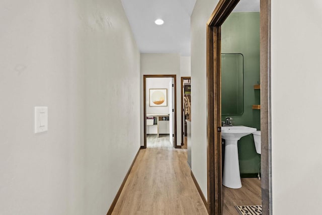 corridor featuring light wood-style floors, baseboards, and a sink