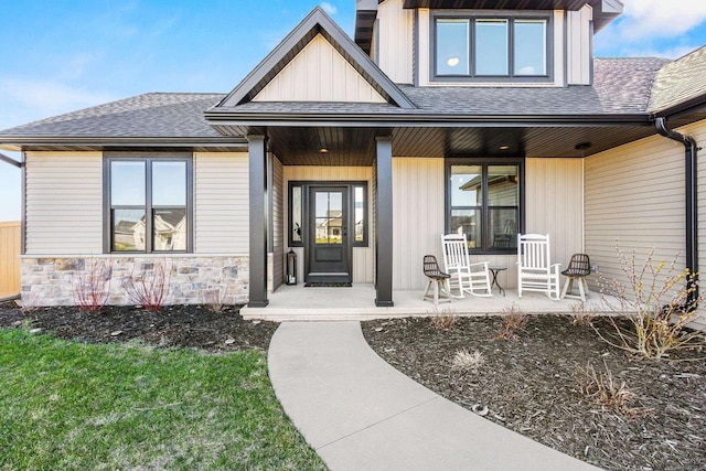 entrance to property featuring a porch, a shingled roof, and stone siding