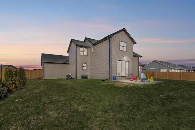 back of property at dusk with a patio, a fenced backyard, central AC, and a yard