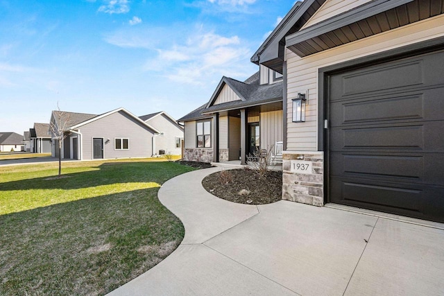 doorway to property featuring a garage, covered porch, stone siding, board and batten siding, and a yard