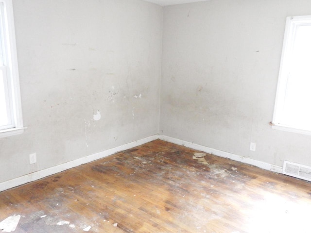 unfurnished room with baseboards, visible vents, a wealth of natural light, and hardwood / wood-style floors