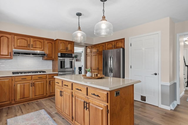kitchen featuring backsplash, pendant lighting, light countertops, light wood-style floors, and stainless steel appliances