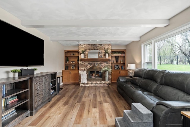 living room featuring a brick fireplace, beam ceiling, and wood finished floors