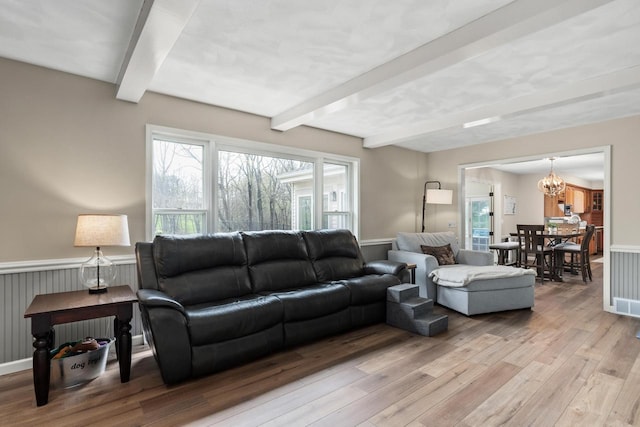 living area with an inviting chandelier, wainscoting, beam ceiling, and light wood-type flooring