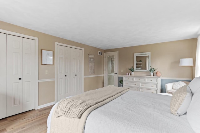 bedroom featuring baseboards, two closets, light wood-type flooring, and visible vents