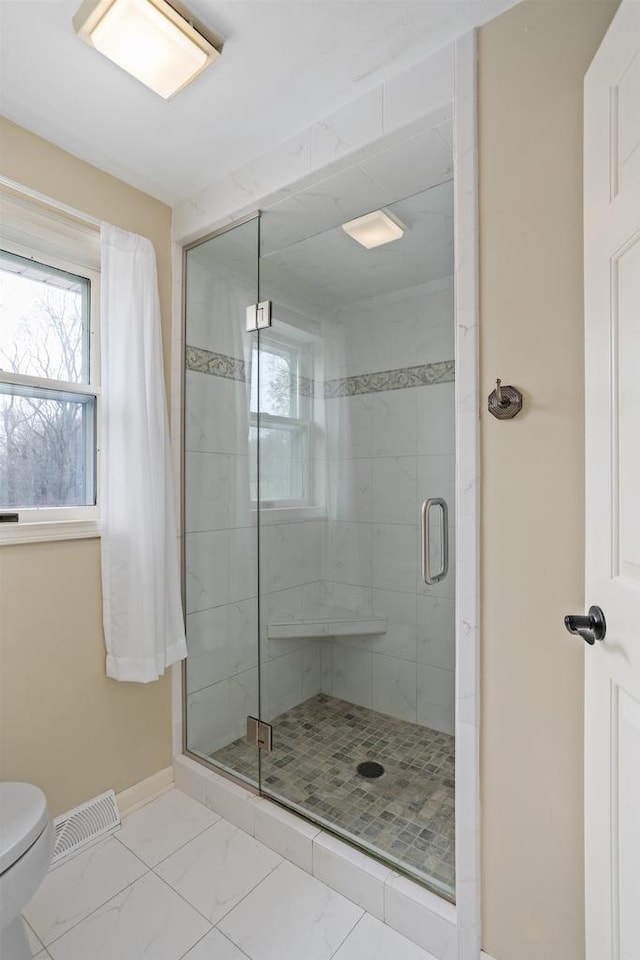 bathroom featuring toilet, visible vents, marble finish floor, and a stall shower