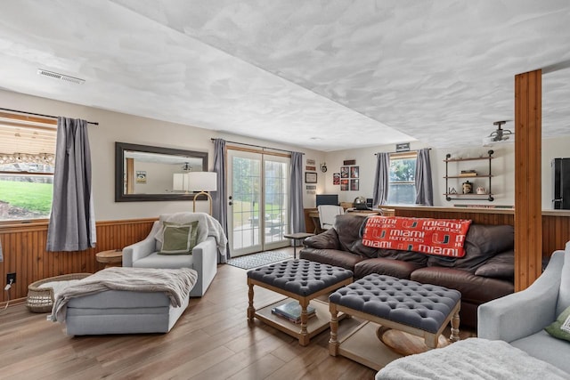living area with visible vents, plenty of natural light, wood finished floors, and a wainscoted wall