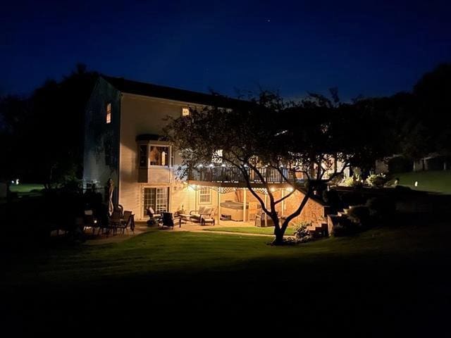 back of house at night featuring a lawn, a patio, and a balcony