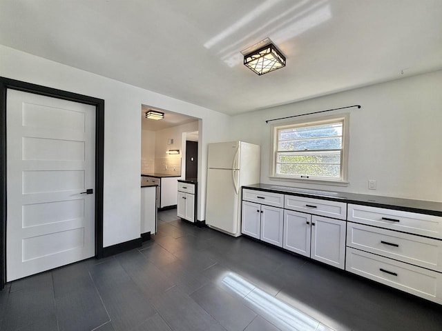kitchen with dark countertops, white cabinets, freestanding refrigerator, and dark tile patterned floors