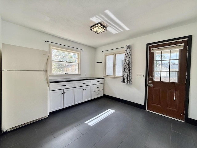 kitchen with baseboards, plenty of natural light, freestanding refrigerator, and white cabinetry