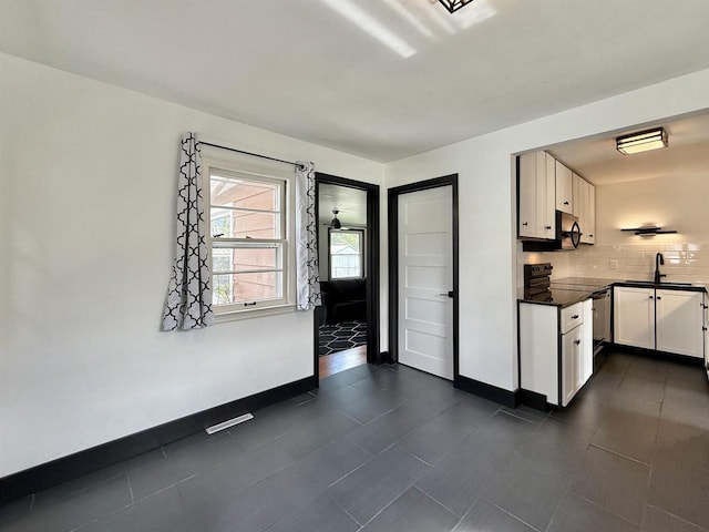 kitchen featuring dark countertops, baseboards, white cabinets, tasteful backsplash, and a sink