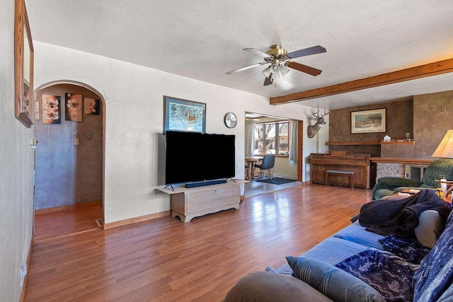 living room with ceiling fan, arched walkways, baseboards, wood finished floors, and beamed ceiling