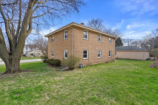 rear view of house featuring a lawn, brick siding, and a chimney