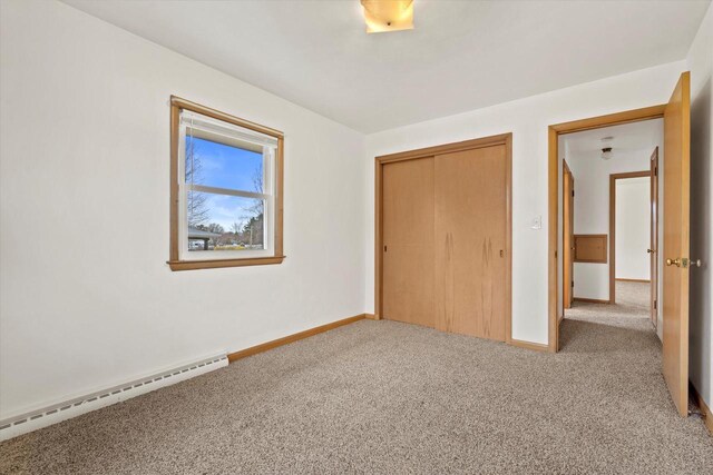 unfurnished bedroom with carpet floors, baseboards, a baseboard heating unit, and a closet