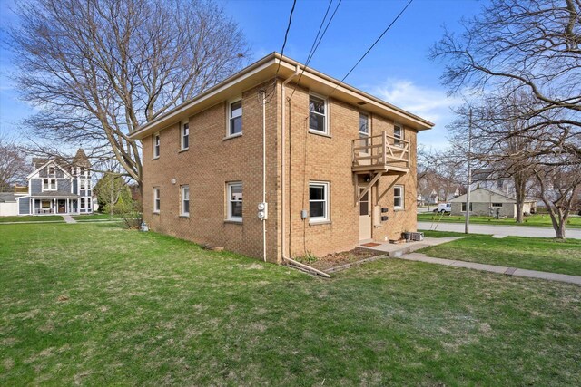 view of side of property with a yard, brick siding, and a balcony