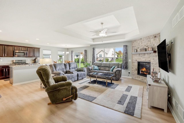 living area with light wood-style floors, ceiling fan, a wealth of natural light, and a stone fireplace