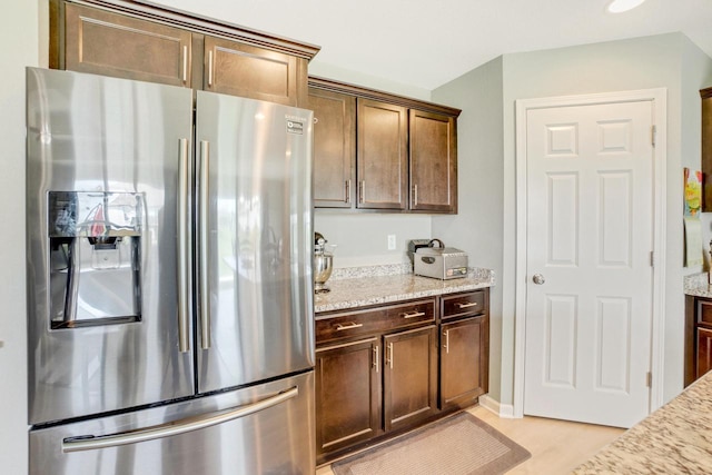 kitchen featuring stainless steel refrigerator with ice dispenser, dark brown cabinetry, and light stone counters