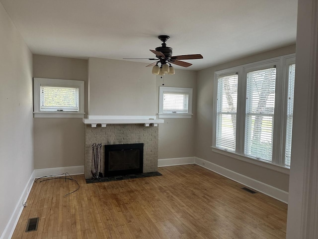 unfurnished living room with baseboards, a brick fireplace, wood finished floors, and visible vents