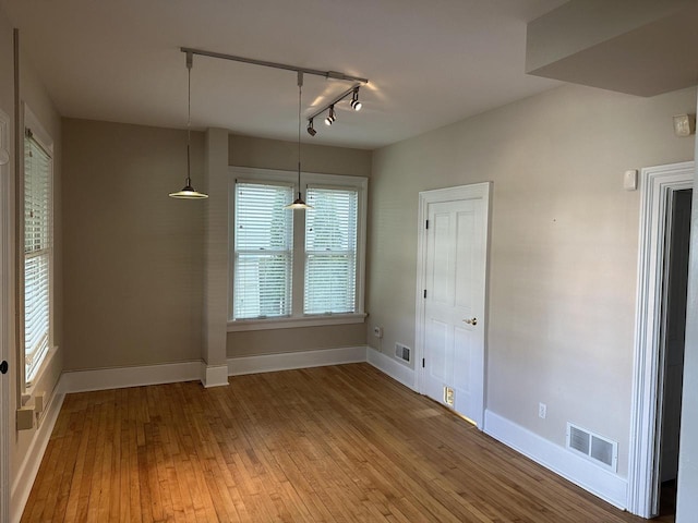 unfurnished dining area featuring visible vents, light wood finished floors, baseboards, and track lighting