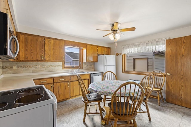 kitchen with decorative backsplash, a ceiling fan, brown cabinets, a sink, and white appliances