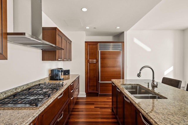 kitchen with wall chimney range hood, stainless steel gas cooktop, a sink, light stone counters, and dark wood-type flooring