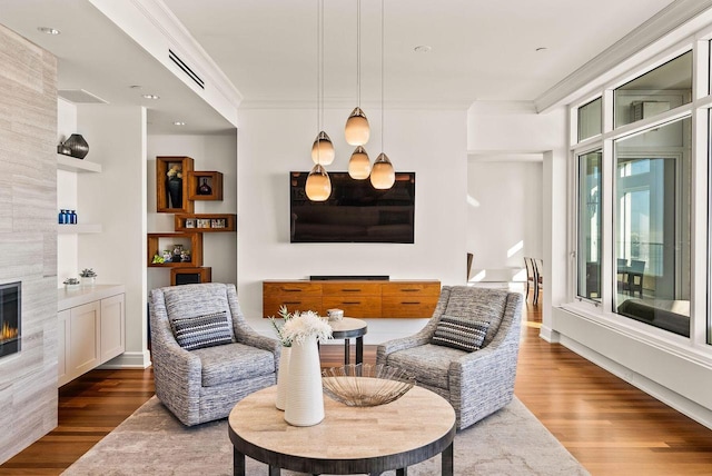 living area featuring visible vents, ornamental molding, a tiled fireplace, and wood finished floors