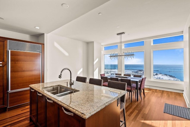 kitchen with a kitchen breakfast bar, dark wood-type flooring, paneled fridge, a chandelier, and a sink