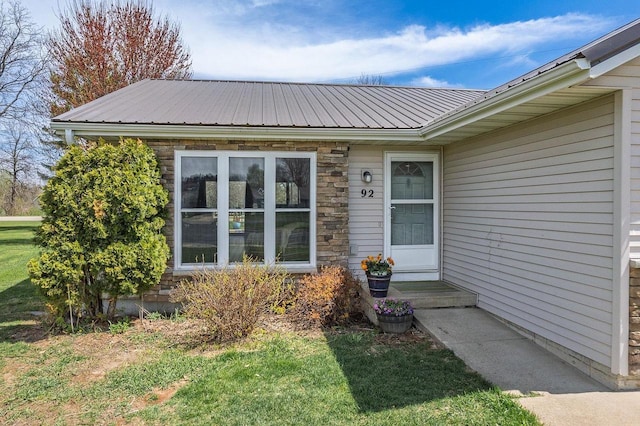 view of exterior entry with a lawn, metal roof, and stone siding