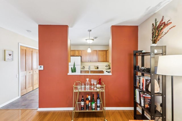 bar with a sink, baseboards, freestanding refrigerator, and decorative light fixtures