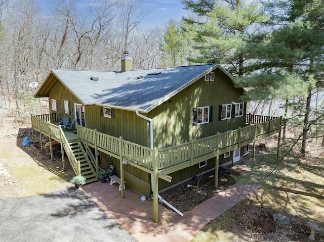 rear view of house featuring a deck, a chimney, stairs, and roof with shingles