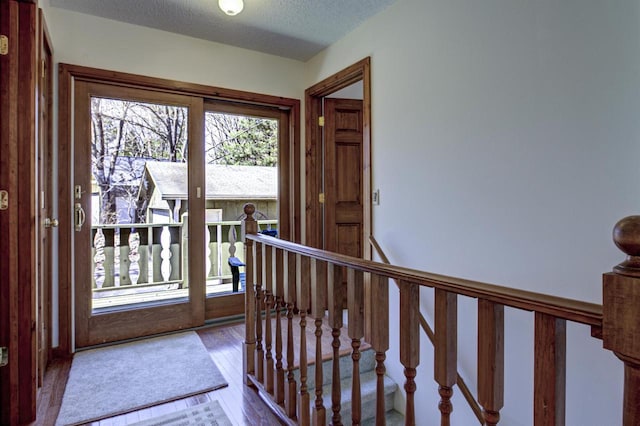 hall with a textured ceiling, an upstairs landing, and wood finished floors