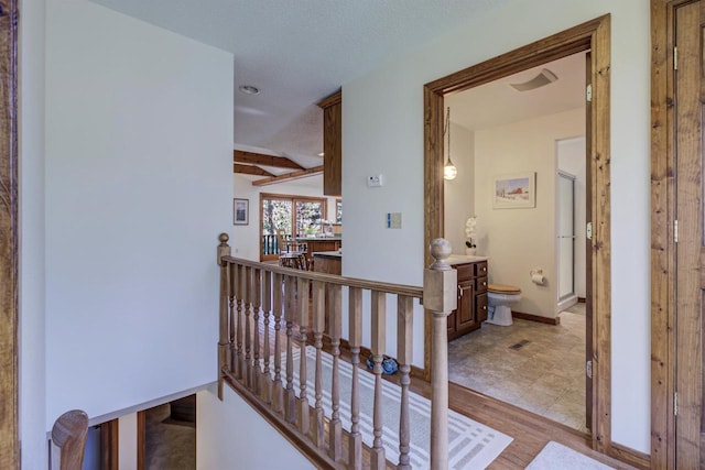 hallway featuring baseboards, light wood-type flooring, beam ceiling, and an upstairs landing
