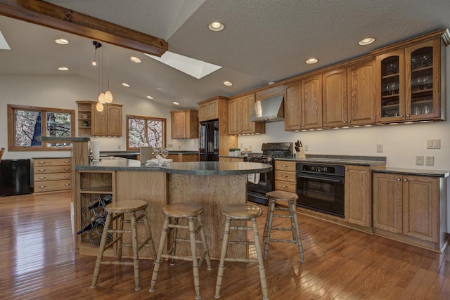 kitchen featuring open shelves, dark countertops, vaulted ceiling with skylight, wall chimney exhaust hood, and black appliances