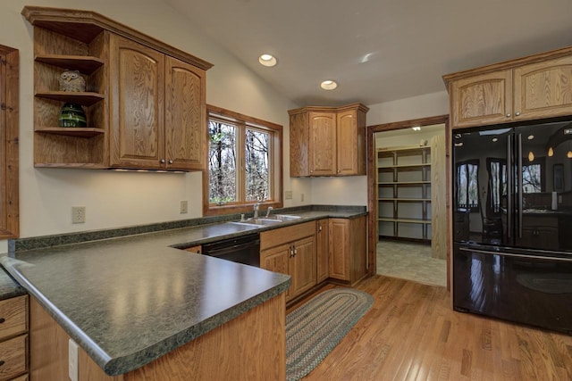kitchen featuring a peninsula, dark countertops, light wood-type flooring, a sink, and black appliances