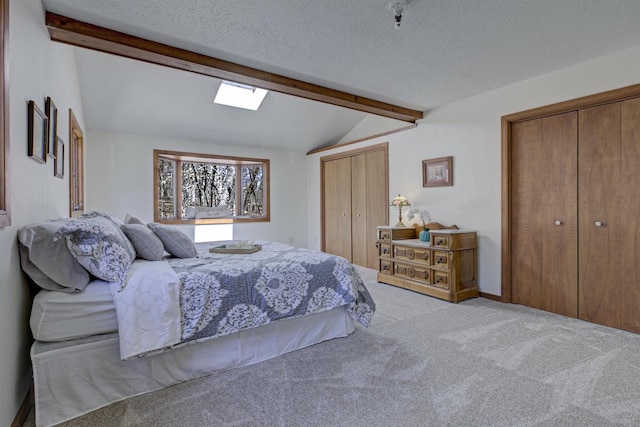 carpeted bedroom with two closets, lofted ceiling with skylight, and a textured ceiling