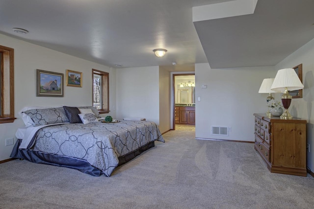 bedroom with baseboards, ensuite bathroom, light colored carpet, and visible vents