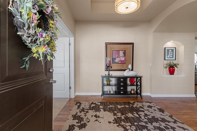 entryway with baseboards, arched walkways, and wood finished floors