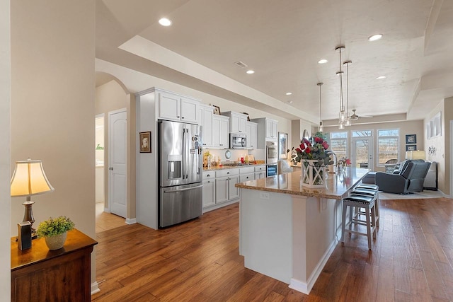 kitchen with dark wood-style flooring, a ceiling fan, appliances with stainless steel finishes, and a kitchen bar