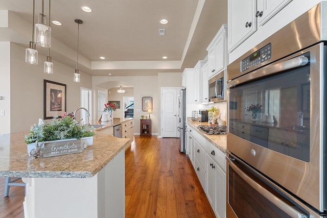 kitchen with white cabinets, a sink, arched walkways, a tray ceiling, and a spacious island